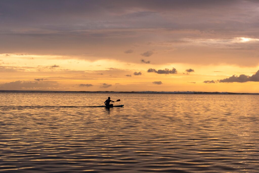 Pessoa remando um caiaque, durante o entardecer.