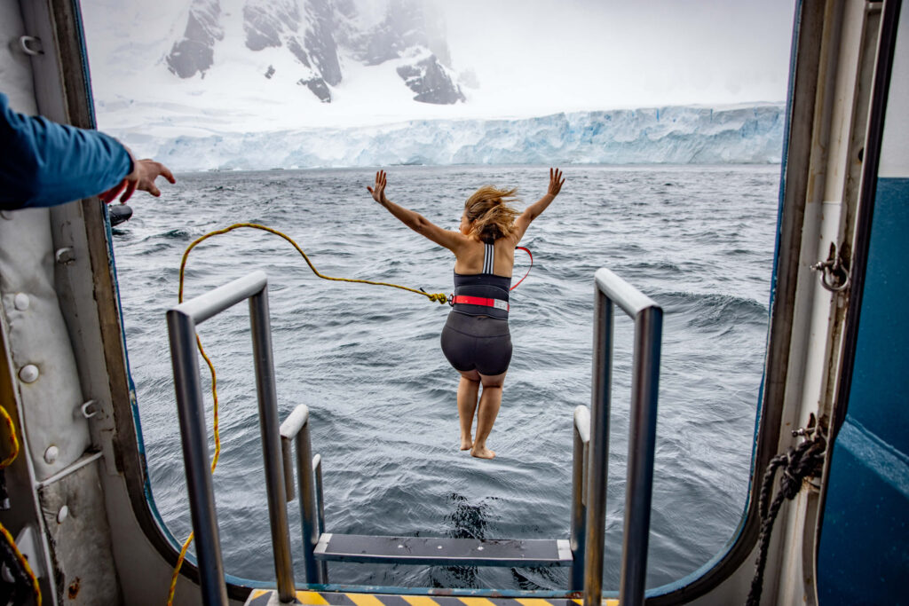 Garanta sua aventura de luxo em alto-mar! Mulher saltando de navio para seu mergulho polar no Ártico, uma das aventuras de luxo em alto-mar da Inguz Expedições.
