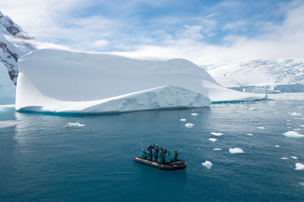 Garanta sua aventura de luxo em alto-mar! Grupo de viajantes navegando de zodiác entre geleiras na Antártica, uma das aventuras de luxo em alto-mar das expedições da Inguz.