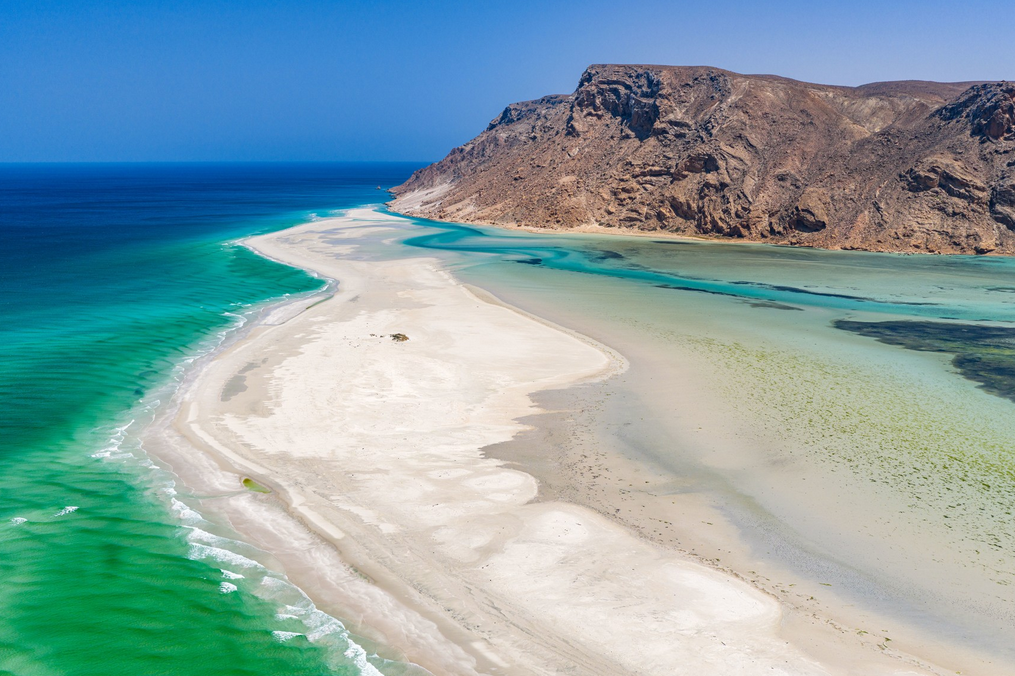 Praia de água cristalina em banco de areia com paredão de rochas ao fundo. Capa de artigo sobre expedições marítimas no blog da Inguz.