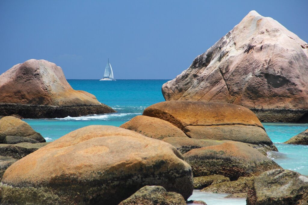 Saiba mais, falando com a Sabine! Rochas banhadas pelas águas azuis da praia em Seychelles.